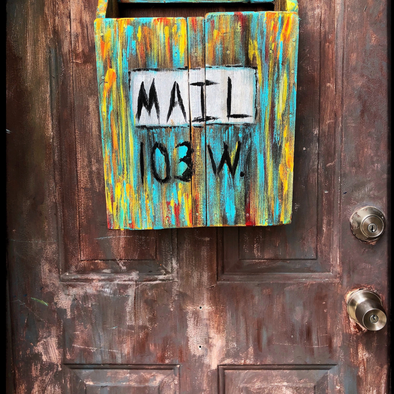 Handpainted artistic mailbox hanging on an old wooden door.